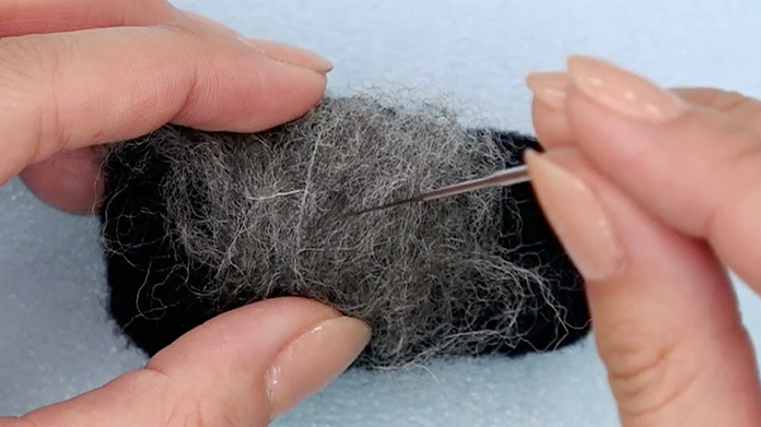タテとヨコの方向に交互に計10回ちぎってグレーの羊毛を混ぜ合わせる。混ぜたグレーの羊毛を黒のベースにのせて刺していく。
