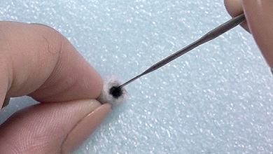 Roll a little black felt between your fingers and poke to attach to the front.