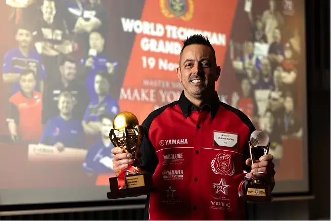 Photo of Liam Coffey smiling while holding a trophy in each hand